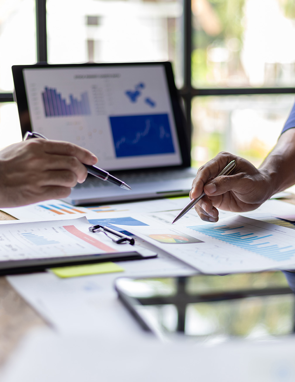 hands with pens point at charts and graphs on table